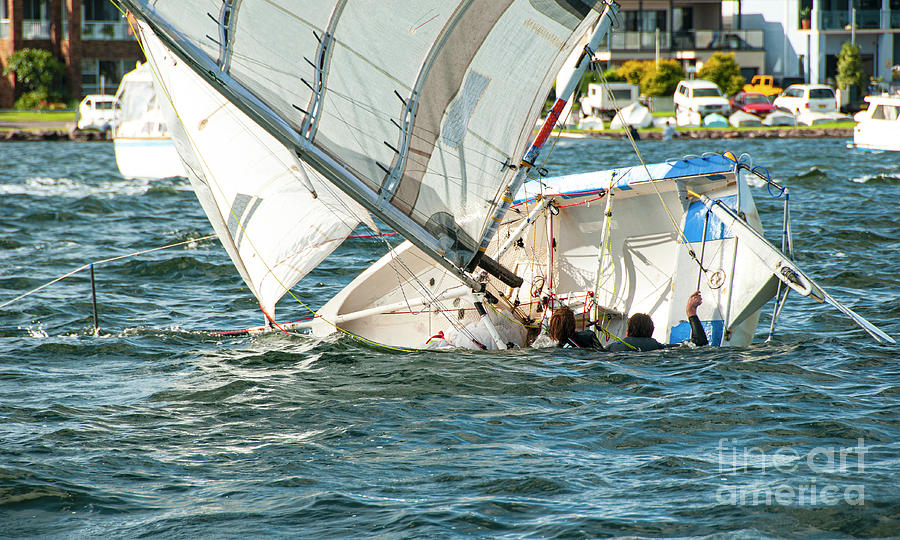 Two children in the water climbing back into a capsized sailboat Photograph by Geoff Childs