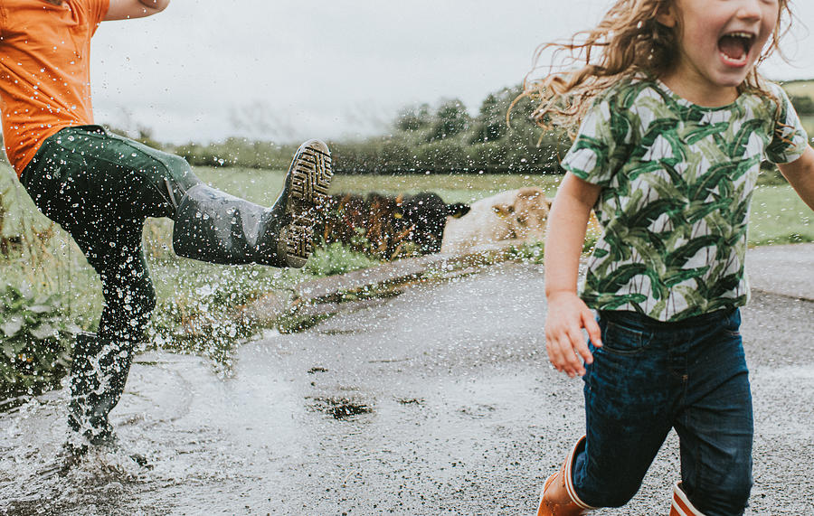 Two children in welly boots play in a Huge Puddle Photograph by Catherine Falls Commercial