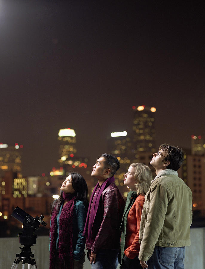 Two couples on rooftop, looking upwards at night sky Photograph by Mike Powell