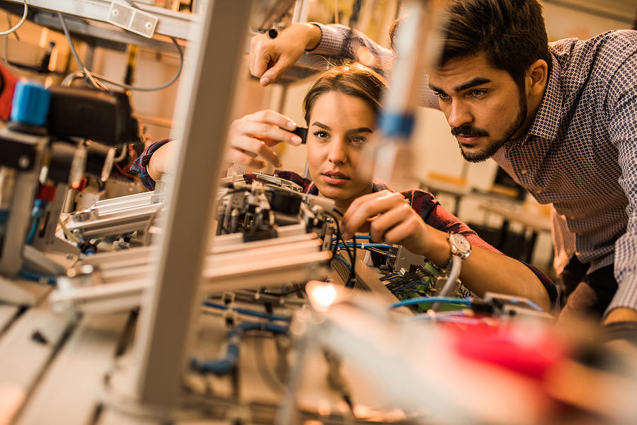 Two engineering students working on electrical component of a machine in laboratory. Photograph by Skynesher