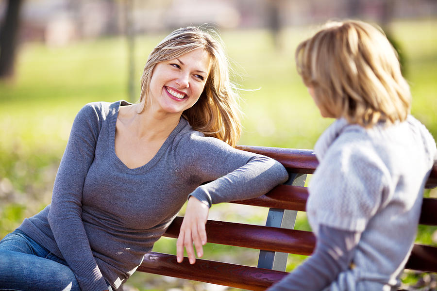 Two female friends talking in a park. Photograph by Skynesher