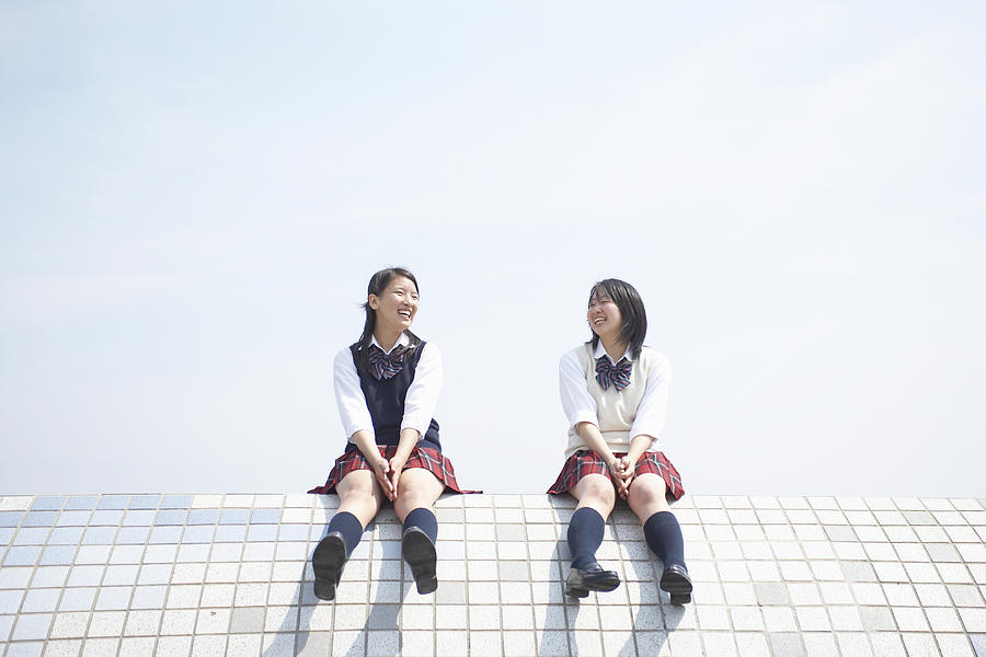 Two female high school students (17-18) sitting on top of tiled wall Photograph by Sot
