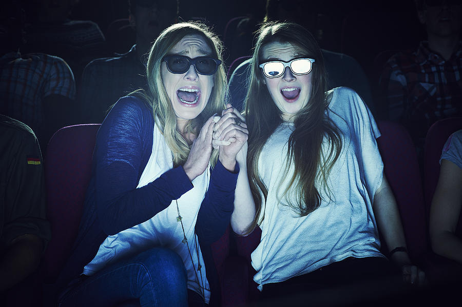 Two girlfriends wearing 3D glasses at the movies Photograph by Flashpop