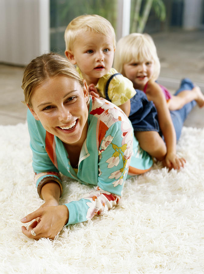 Two girls (21-24 months) on womans back, lying on rug, smiling Photograph by Kraig Scarbinsky