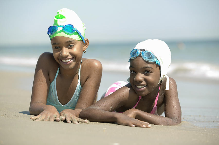 Two girls (8-9) lying on beach, smiling, portrait, (focus on foreground) Photograph by Gregory Costanzo