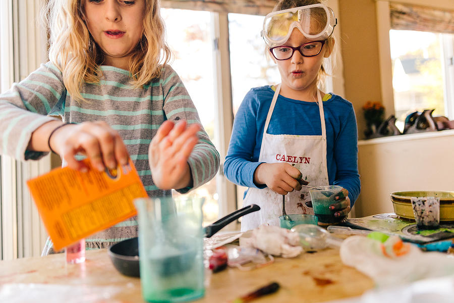 Two girls doing science experiment, pouring packet into frying pan Photograph by Heshphoto