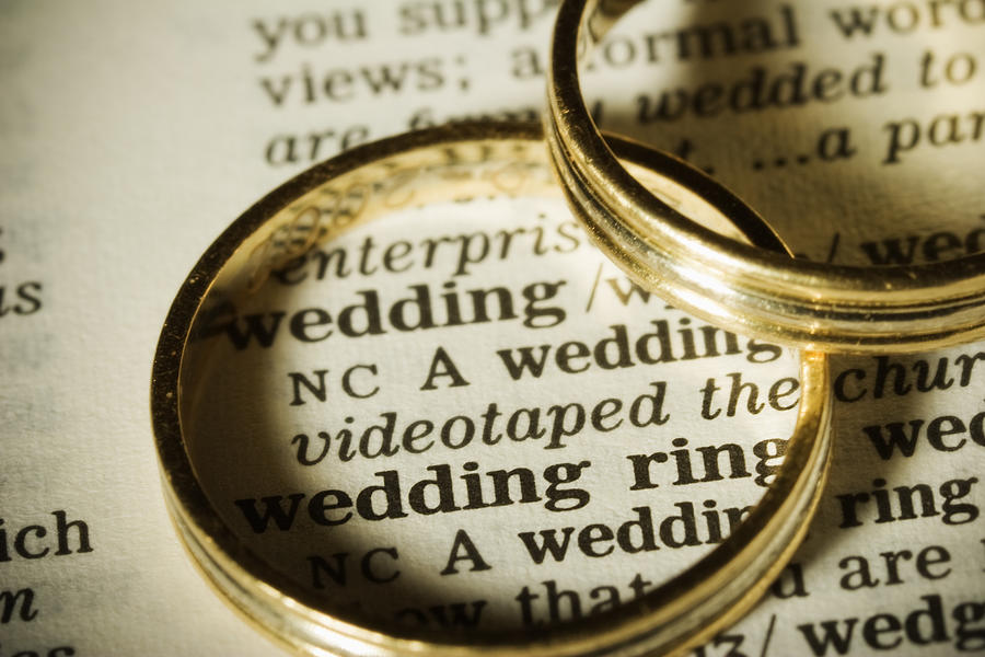 Two gold wedding bands on top of paper with the word wedding Photograph by JLGutierrez