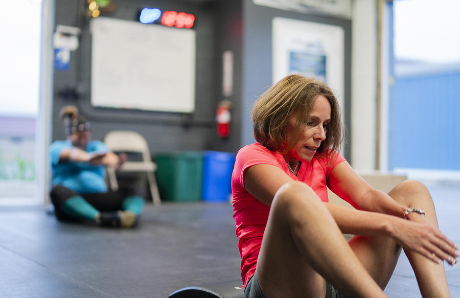 Two Hispanic women, the senior 55-years-old on the front and the young body-positive in the background, doing exercise in the gym Photograph by Alex Potemkin