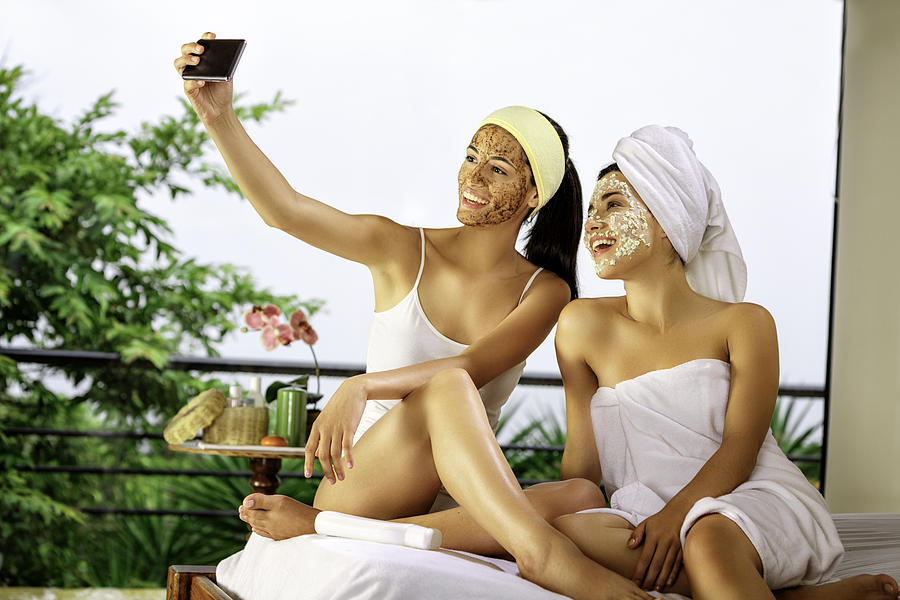 Two Hispanic young woman taking a selfie while doing beauty treatments at home or spa. Photograph by Apomares