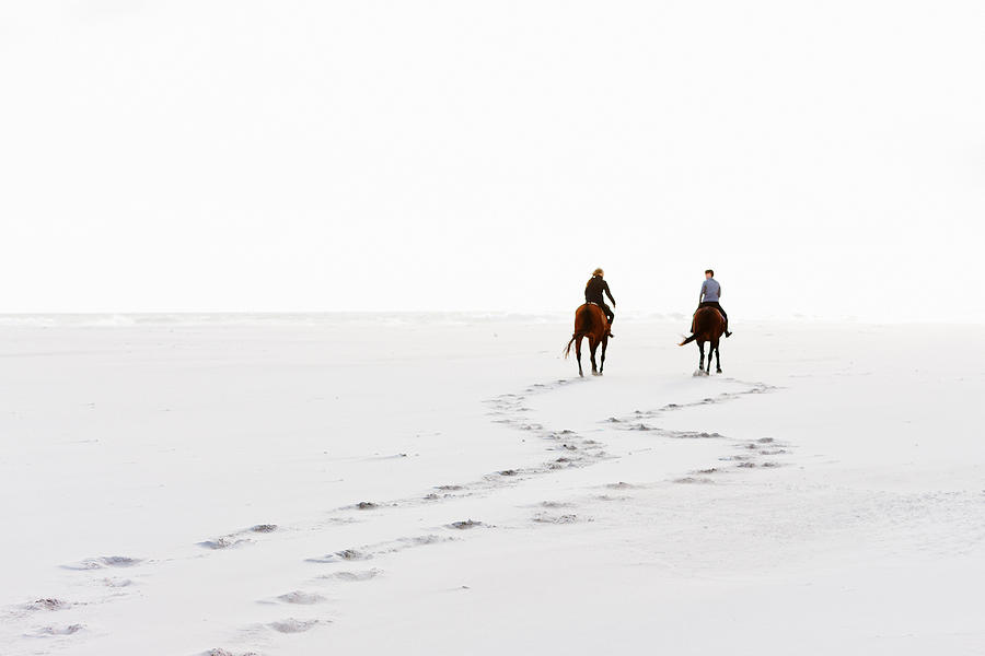 Two horseriders leave hoofprints in the sand on winter day Photograph by RapidEye