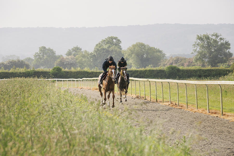 Two horses and riders on a gallops path, racing against each other in a training exercise. Racehorse training.  Photograph by Mint Images