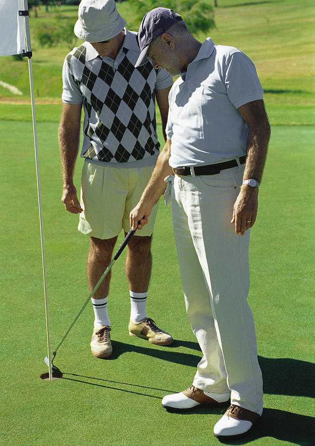Two mature golfers looking at hole Photograph by Vincent Hazat
