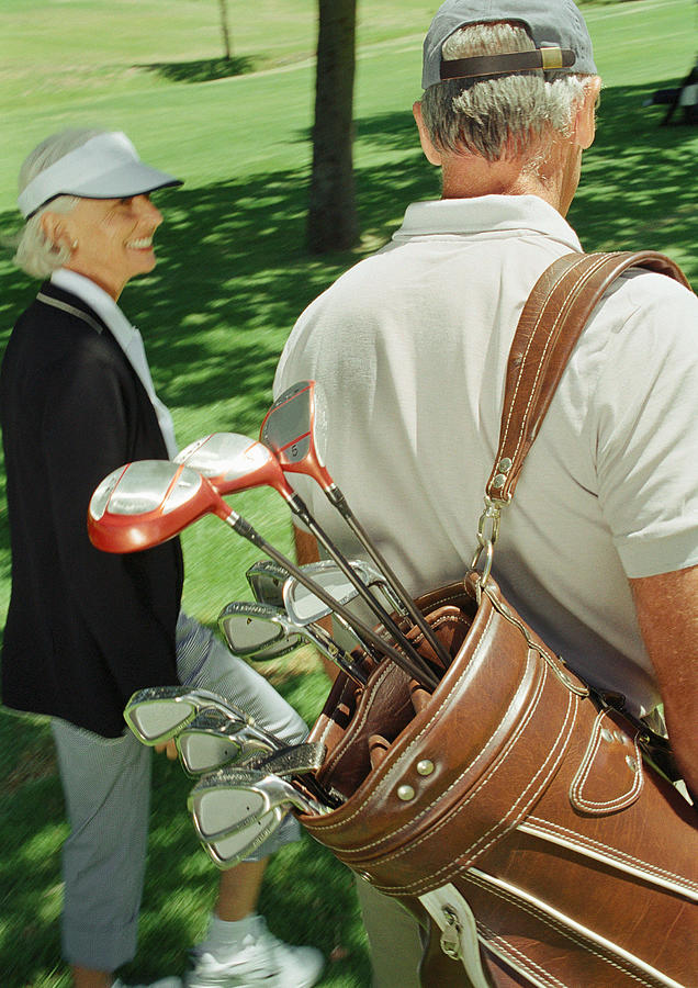 Two mature golfers, one carrying clubs, rear view Photograph by Vincent Hazat