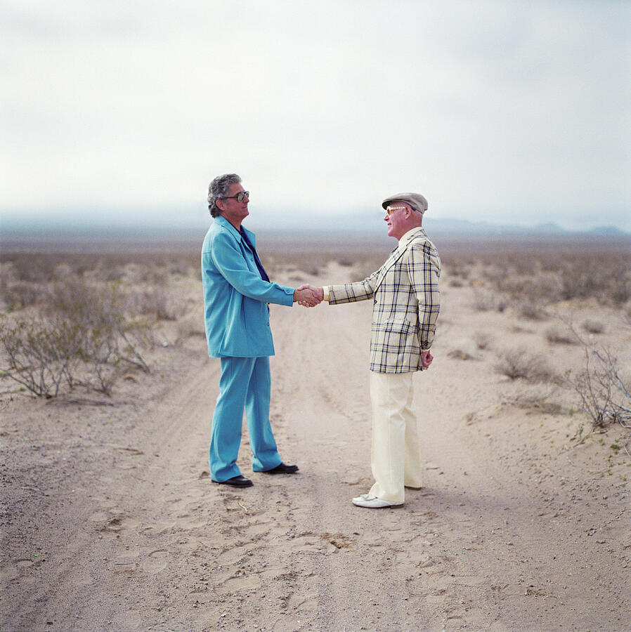 Two mature men in suits shaking hands in the desert Photograph by Pnc