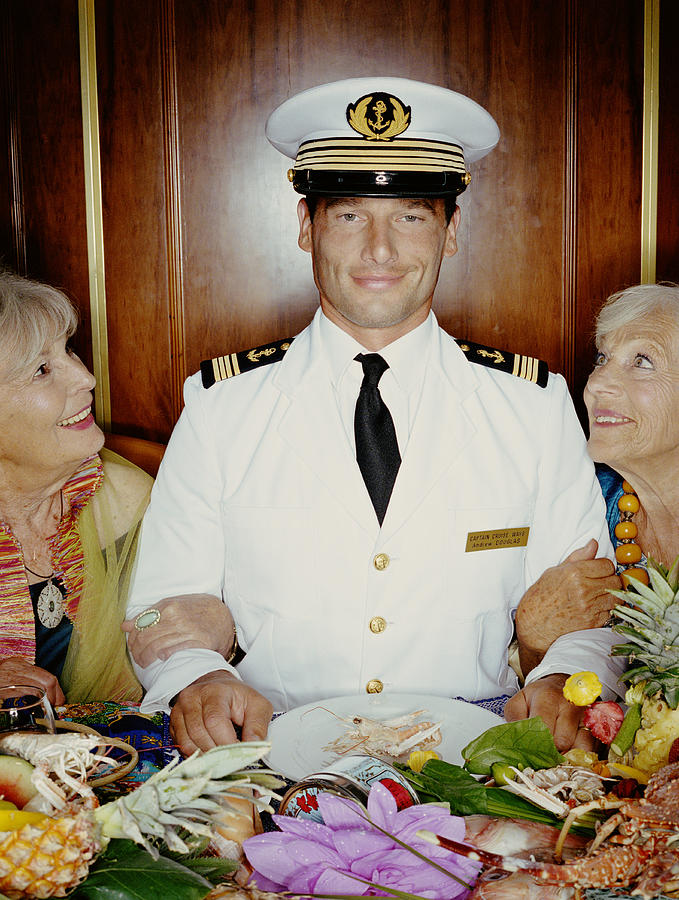 Two mature women arm in arm with captain at table, smiling, portrait Photograph by Britt Erlanson