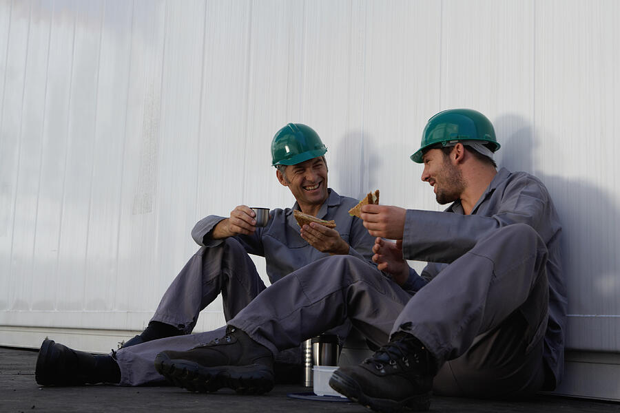 Two men eating lunch beside cargo container, wearing hard hats Photograph by Tay Jnr