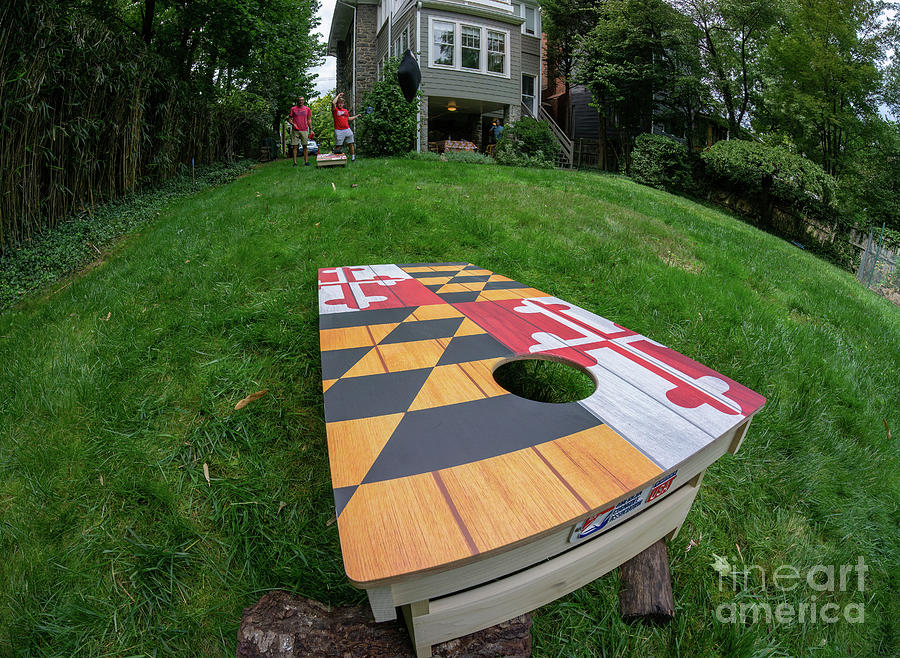 Two men play cornhole on a board with a Maryland flag motif in a Photograph by William Kuta