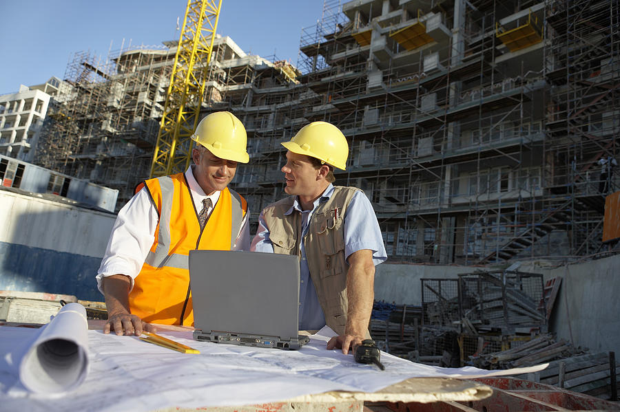 Two Men Wearing Hard Hats Looking at a Laptop Computer on a Building Site Photograph by Digital Vision.