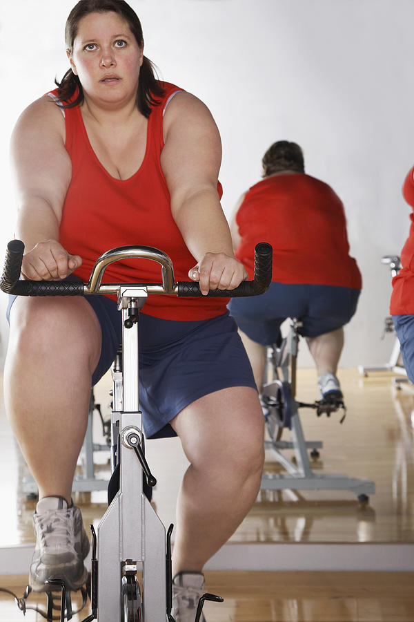 Two overweight women on exercise bike in gym Photograph by Gravity Images