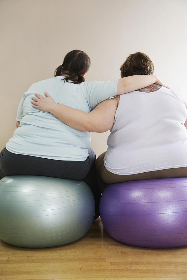 Two overweight women sitting on fitness ball, rear view Photograph by Gravity Images