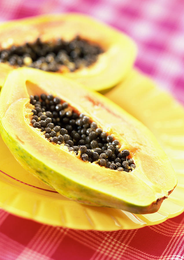 Two papaya halves on yellow plate, close-up Photograph by Jean-Blaise Hall
