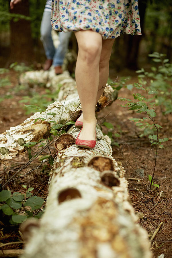 Two people walking along a fallen tree trunk in the woods. Photograph by Mint Images - Jonathan Kozowyk