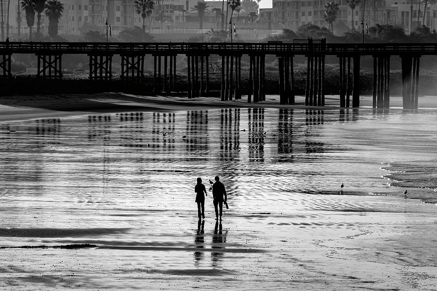 Two poeple walking on the beach heading toward the pier Photograph by Dan Friend