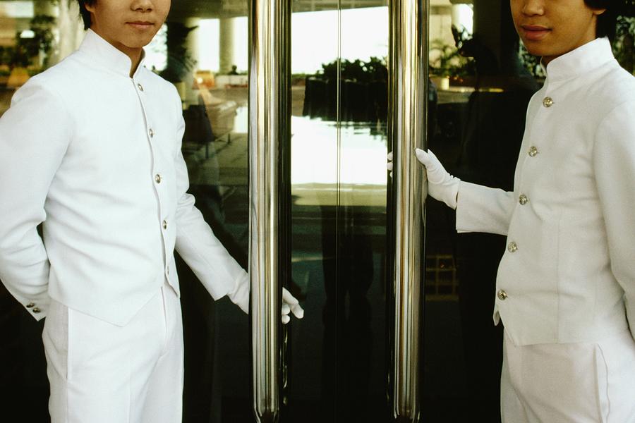 Two porters standing at the entrance of a hotel doors, Regent Hotel, Kowloon, Hong Kong, China Photograph by Glowimages