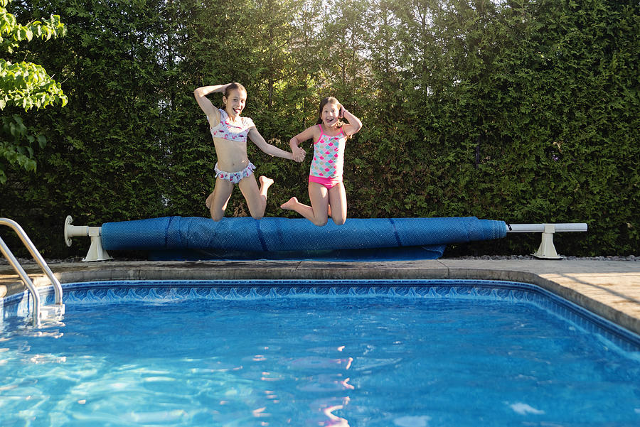 Two preteen girls jumping in pool making faces. Photograph by Martinedoucet