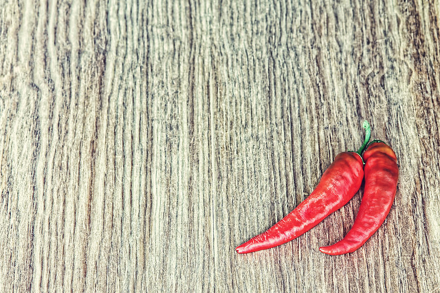 Two Red Hot Chili peppers on grunge wooden background.Toned image. Photograph by Grotmarsel