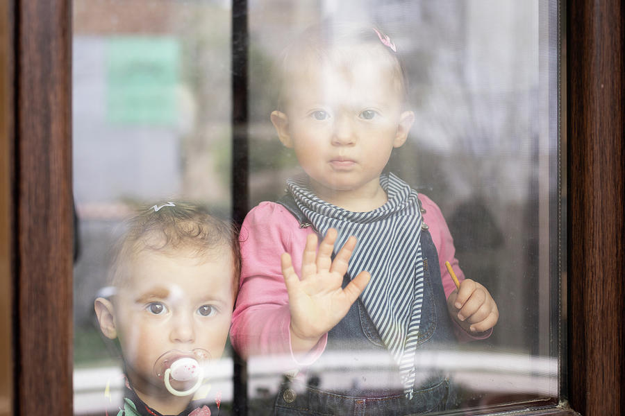 Two Sad Baby Girl Twins Staring Out The Window. Stay At Home Quarantine Coronavirus Pandemic Prevention. Photograph
