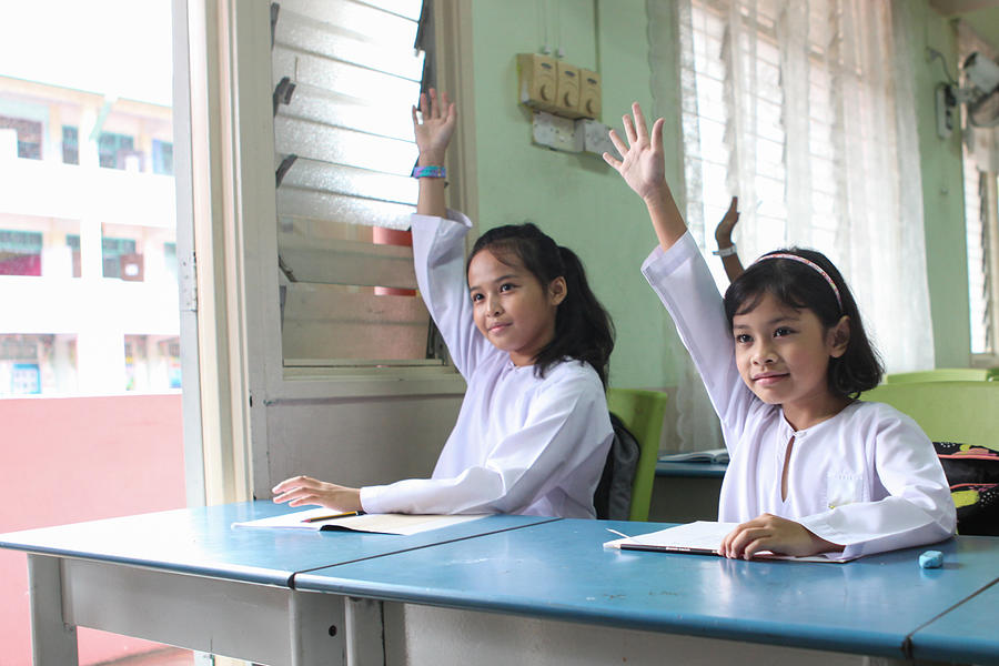 Two Schoolgirls Raising Their Hands in A Classroom Photograph by Faidzzainal