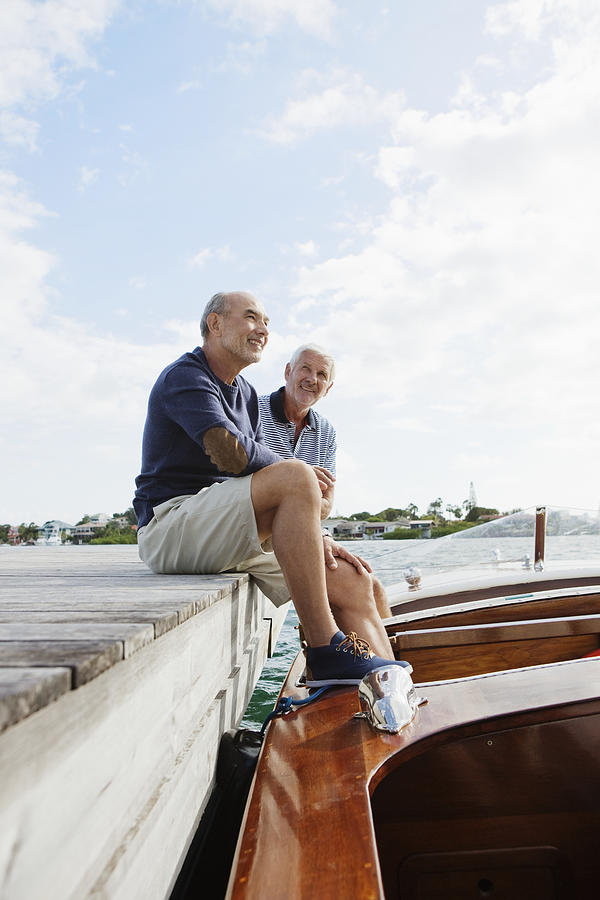 Two senior friends resting on jetty with moored motorboat Photograph by Felix Wirth