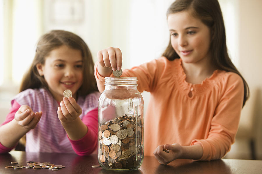 Two Sisters putting coins in a jar Photograph by SelectStock