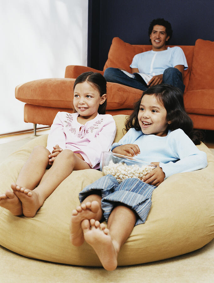 Two Sisters Watching TV With Their Father in Their Living Room Photograph by Digital Vision.