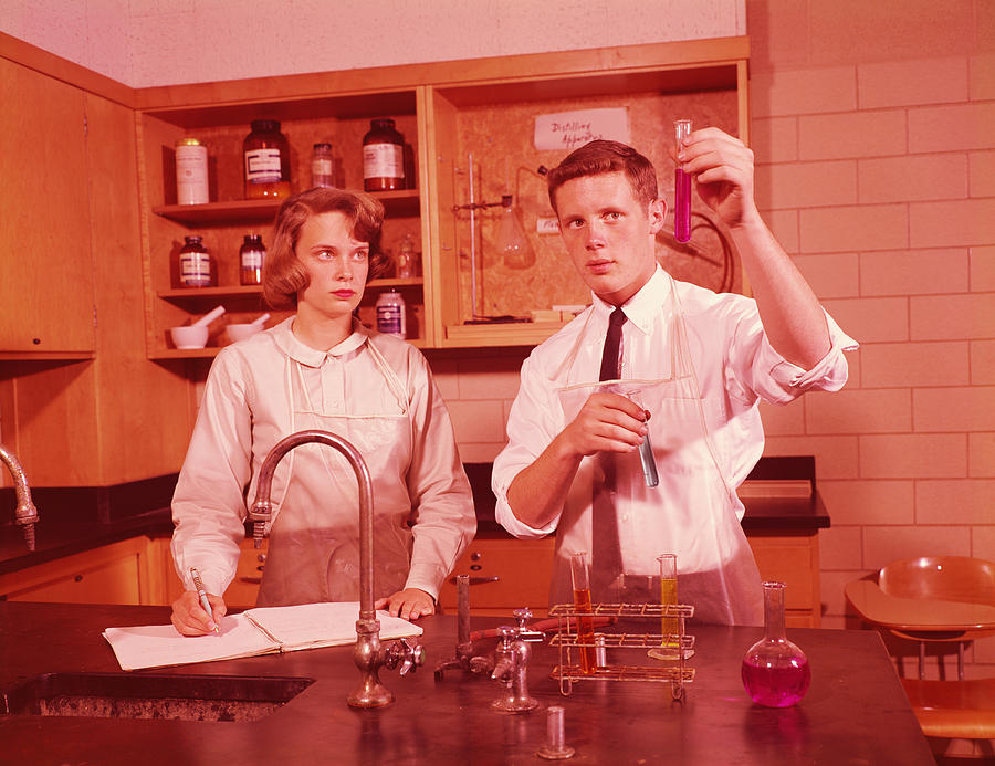 Two students in chemistry laboratory, conducting experiment, boy holding test-tube, girl making notes. Photograph by H. Armstrong Roberts