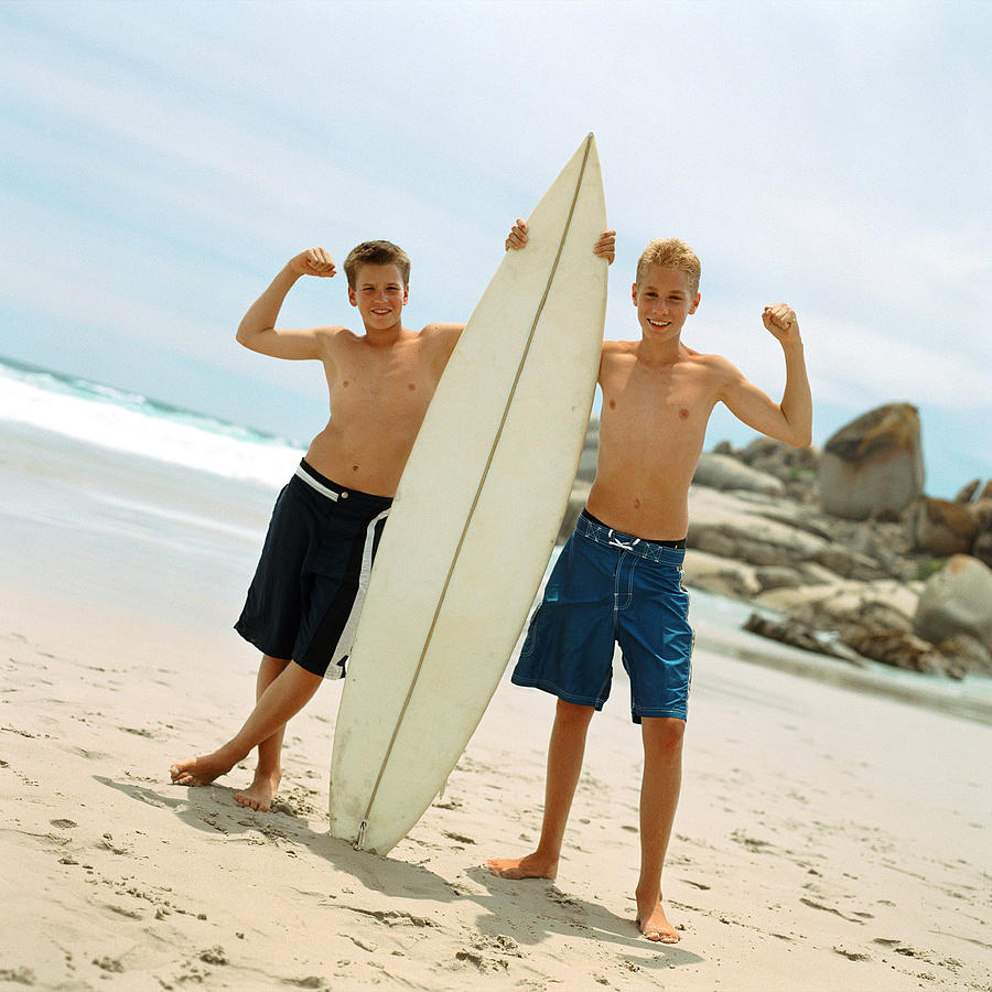 Two teenage boys on beach holding surfboard Photograph by Patrick Sheandell OCarroll