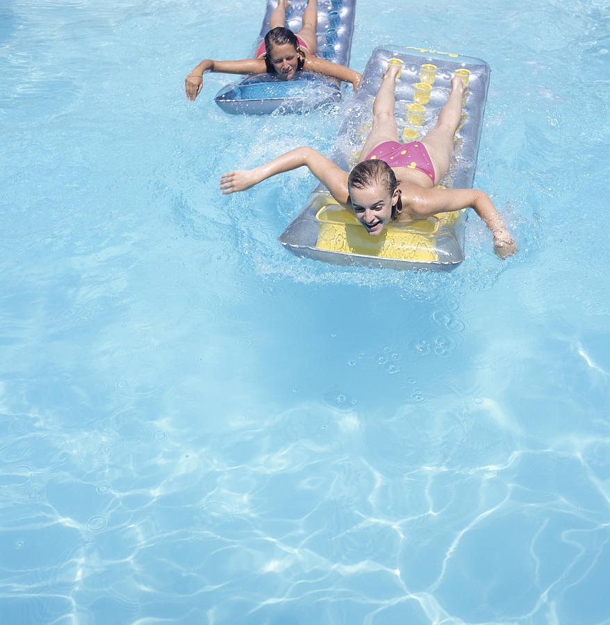 Two teenage girls (16-17) floating face down on airbeds in pool, elevated view Photograph by David De Lossy