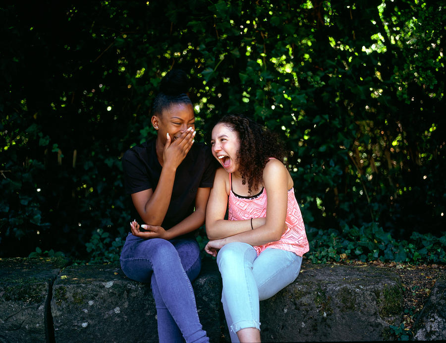 Two teenage girls laughing together in a park Photograph by Alys Tomlinson