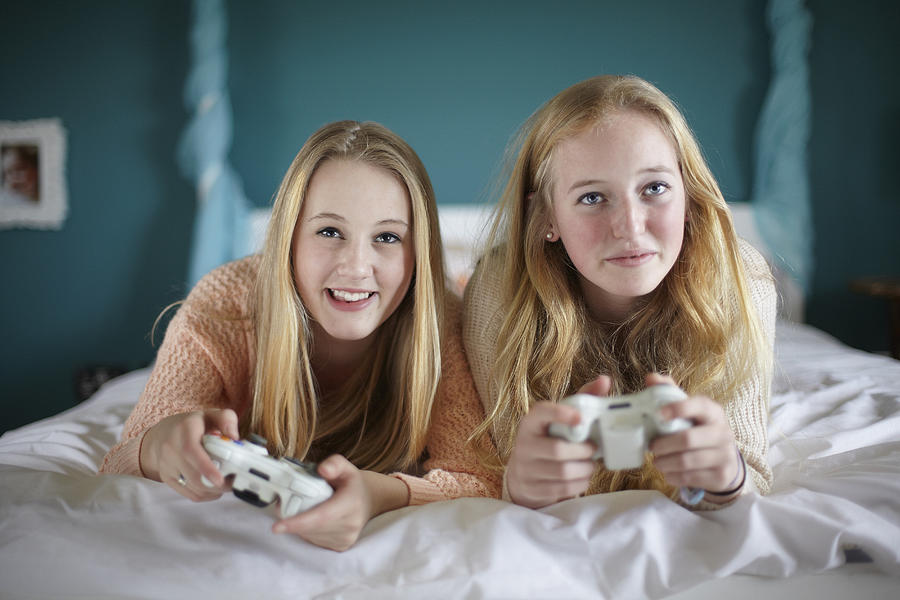 Two teenage girls playing on computer game in bedroom Photograph by Tim Macpherson