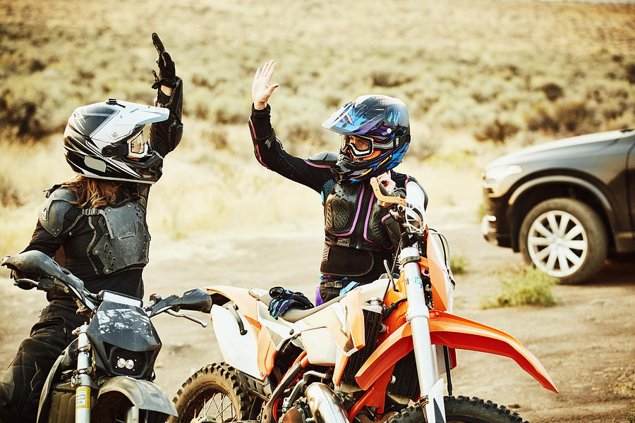 Two women high fiving after dirt bike ride in desert Photograph by Thomas Barwick