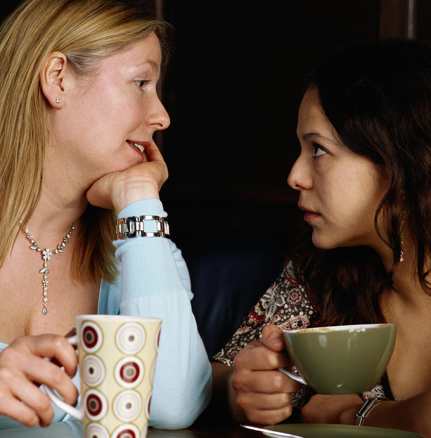 Two women holding drinks, looking at each other, close-up Photograph by Dana Neely
