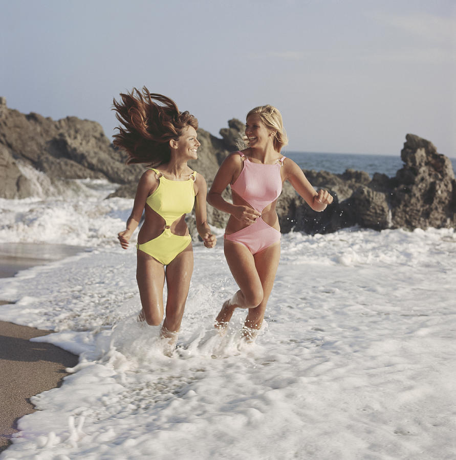 Two women in swimwear running on beach, smiling Photograph by Tom Kelley Archive