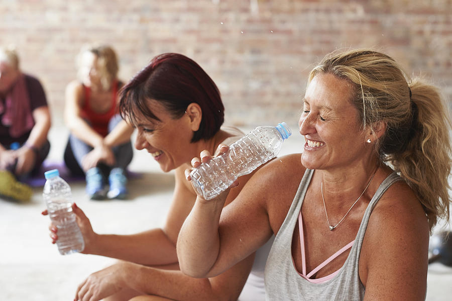 Two women laughing and drinking from water bottles in the gym Photograph by Richard Drury
