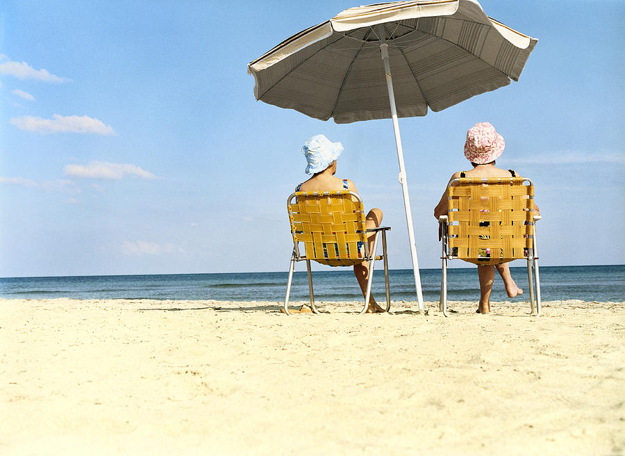 Two Women Sitting a Chairs Under a Parasol on the Beach Photograph by Digital Vision.