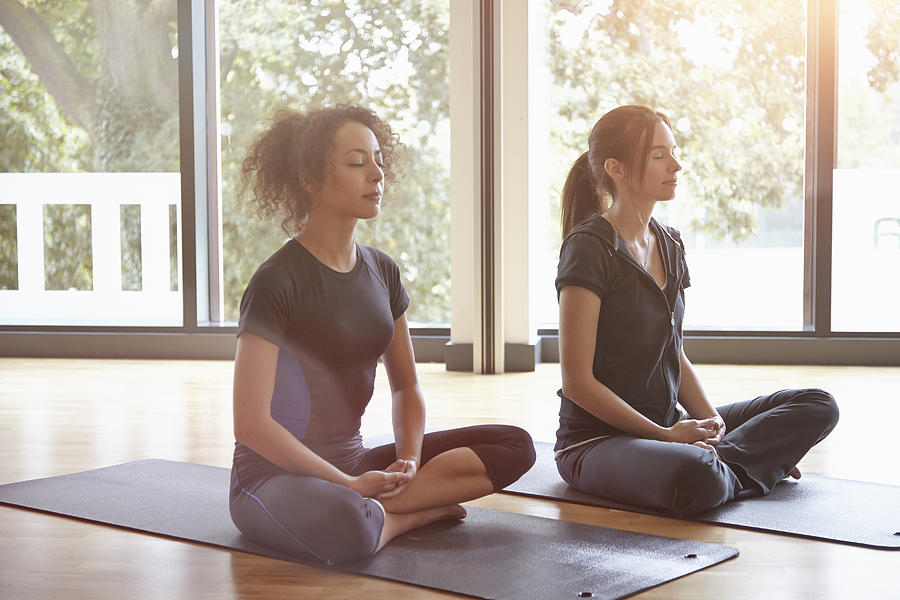 Two women sitting in a yoga class meditating Photograph by 10000 Hours