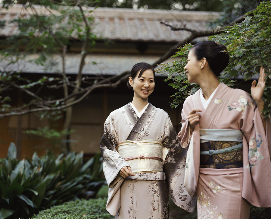 Two Women Wearing a Kimono Standing in a Garden, One Waving Goodbye Photograph by Digital Vision.