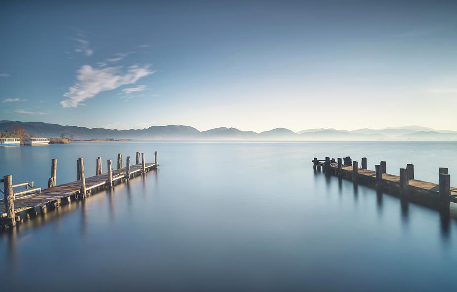 Two Wooden pier or jetty at sunset and sky reflection on water.  Photograph by Stefano Orazzini