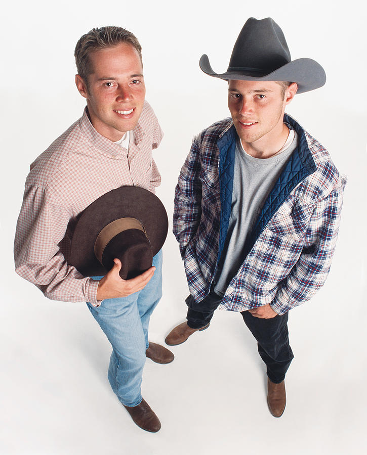 Two Young Adult Caucasian Cowboys Wearing Boots Are Standing Beside Each Other One Holding A Hat And One Wearing A Hat Photograph by Photodisc