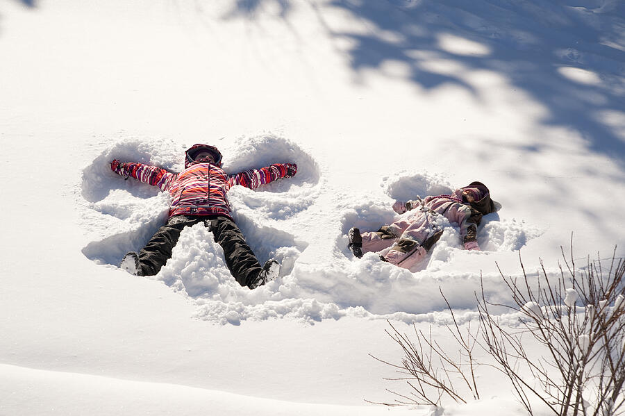 Two young girls doing snow angels, full length horizontal. Photograph by Martinedoucet